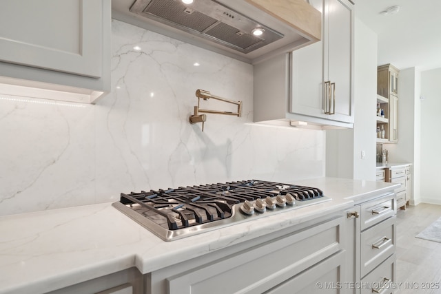 8499 S Timber Wolf Dr, Broken Arrow, OK 74014 - kitchen featuring premium range hood, stainless steel gas cooktop, backsplash, light stone counters, and light wood-style floors