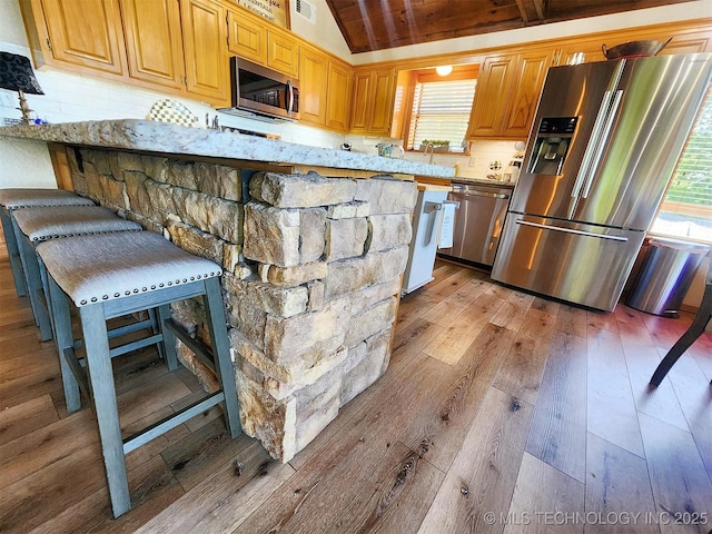 35824 S Talon Dr, Cookson, OK 74427 - kitchen featuring appliances with stainless steel finishes, light wood finished floors, vaulted ceiling, tasteful backsplash, and a kitchen bar