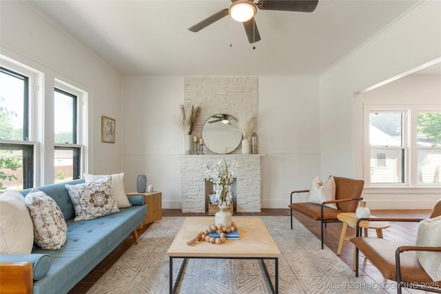 living area with plenty of natural light, wood finished floors, crown molding, a stone fireplace, and ceiling fan