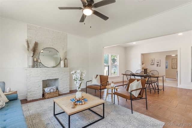 living room featuring a ceiling fan, ornamental molding, baseboards, and a stone fireplace
