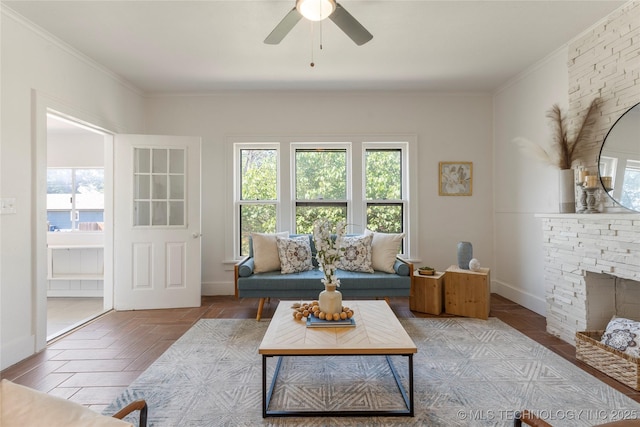 living area with plenty of natural light, crown molding, a ceiling fan, and baseboards
