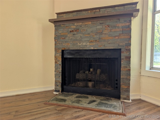 detailed view of a fireplace, wood finished floors, and baseboards