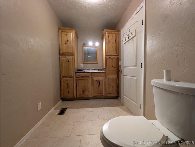 bathroom featuring toilet, tile patterned floors, a textured ceiling, a textured wall, and vanity
