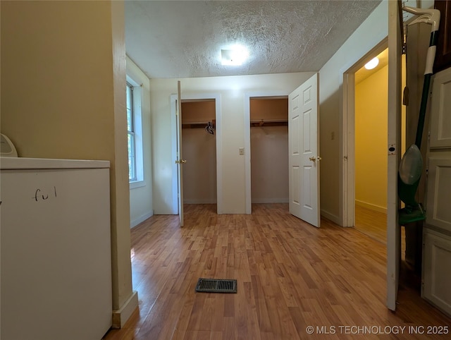 unfurnished bedroom featuring fridge, multiple closets, light wood finished floors, a textured ceiling, and baseboards