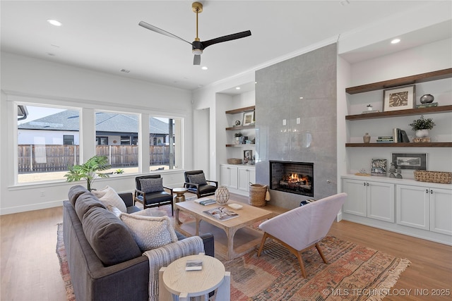living room with built in features, healthy amount of natural light, light wood finished floors, crown molding, and recessed lighting