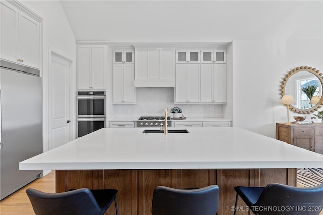 kitchen featuring appliances with stainless steel finishes, a sink, tasteful backsplash, a kitchen bar, and light countertops