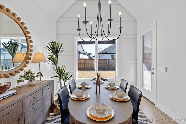 dining space featuring vaulted ceiling, a chandelier, light wood-style floors, and wood walls
