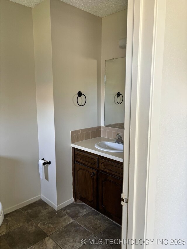 1612 Rustic Dr, Ardmore, OK 73401 - bathroom featuring vanity, decorative backsplash, toilet, a textured ceiling, and baseboards