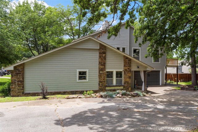6315 E 98th Pl, Tulsa, OK 74137 - view of property exterior featuring driveway, an attached garage, a chimney, stone siding, and fence