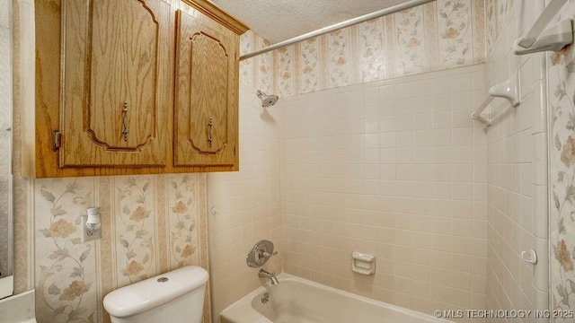 bathroom featuring toilet, shower / washtub combination, wallpapered walls, and a textured ceiling