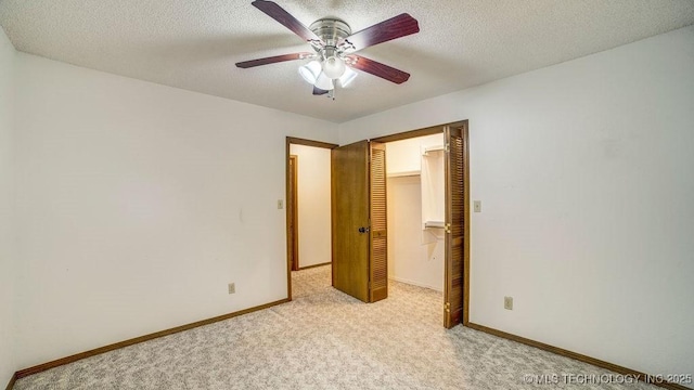 unfurnished bedroom with light colored carpet, a walk in closet, baseboards, a textured ceiling, and a closet
