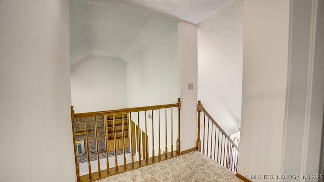 corridor with an upstairs landing, carpet flooring, a textured ceiling, and lofted ceiling