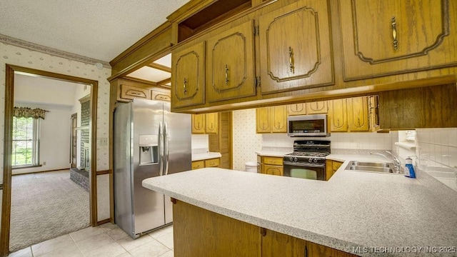 kitchen featuring stainless steel appliances, wallpapered walls, light countertops, a sink, and a peninsula