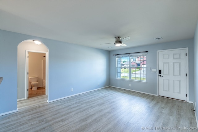 unfurnished living room featuring wood finished floors, arched walkways, a ceiling fan, and baseboards