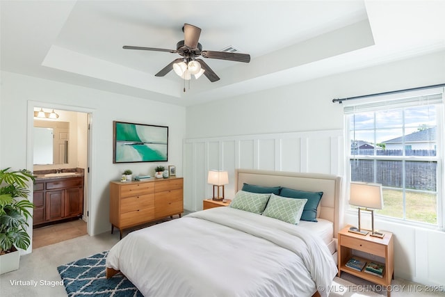 bedroom featuring a raised ceiling, multiple windows, ensuite bath, and a ceiling fan