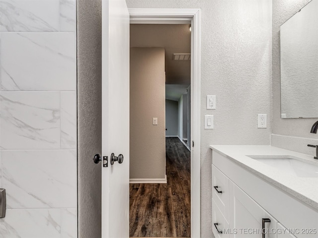 bathroom with wood finished floors, vanity, baseboards, and a textured wall