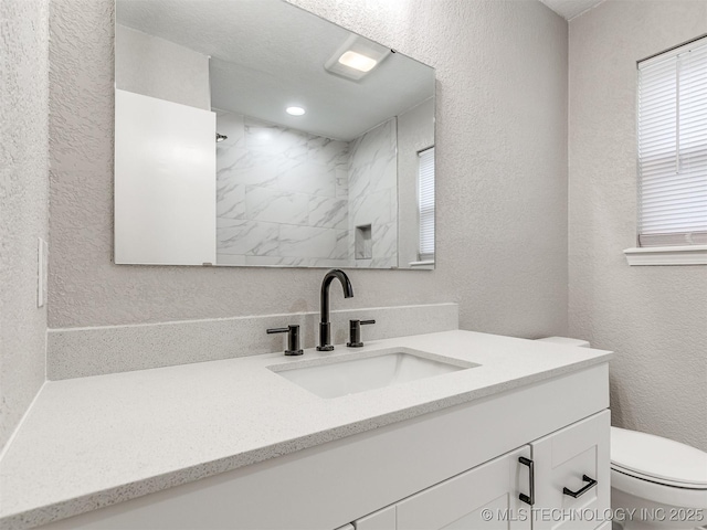 bathroom featuring vanity, toilet, a textured wall, and walk in shower