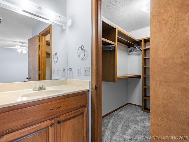 1044 Meadow Dr, Bartlesville, OK 74006 - bathroom featuring vanity, baseboards, a spacious closet, ceiling fan, and a textured ceiling