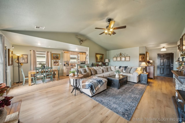 living room with a ceiling fan, lofted ceiling, and light wood-style floors