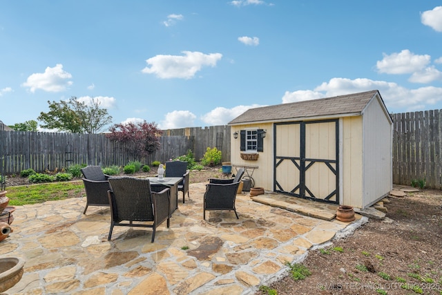 view of patio / terrace with outdoor dining space, a storage unit, a fenced backyard, and an outbuilding