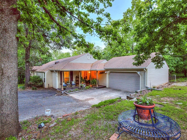 ranch-style home featuring covered porch, an attached garage, concrete driveway, and a shingled roof