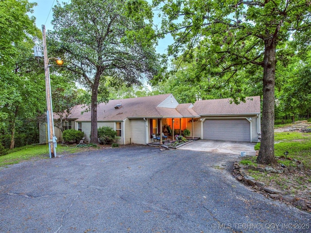 view of front of house with driveway, a garage, covered porch, and roof with shingles