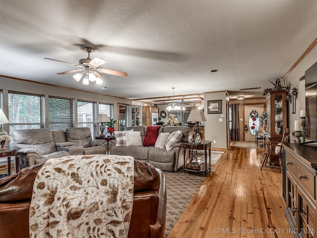 living area with light wood finished floors, a textured ceiling, a ceiling fan, ornamental molding, and a chandelier