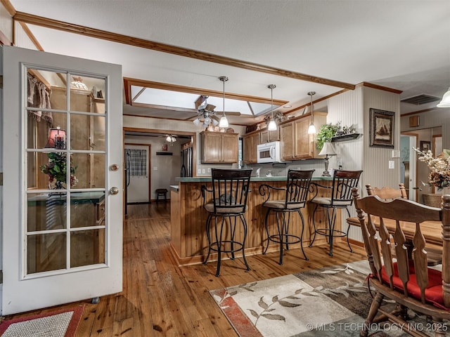 kitchen with white microwave, ornamental molding, wood-type flooring, a peninsula, and black refrigerator