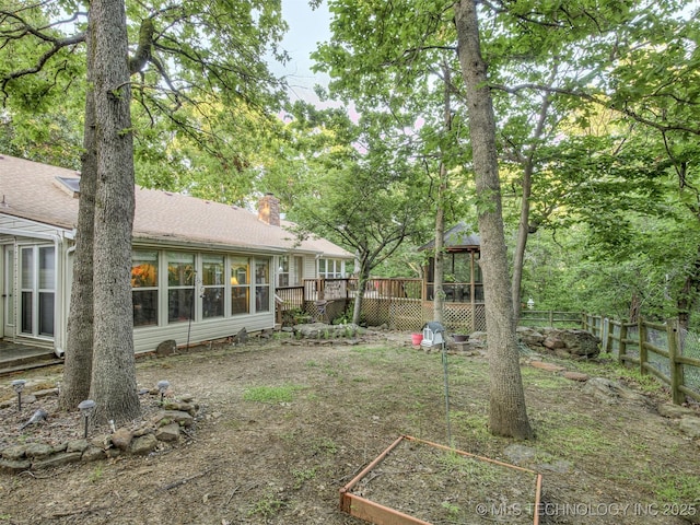 view of yard with a deck, fence, a vegetable garden, and a sunroom