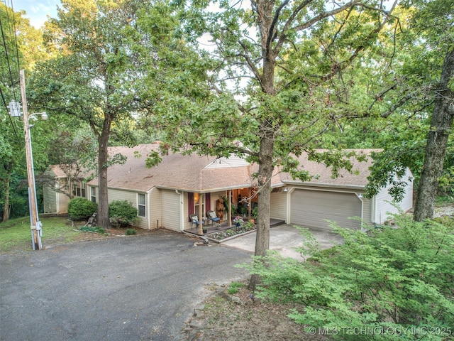 view of front of property featuring asphalt driveway, an attached garage, a shingled roof, and a porch