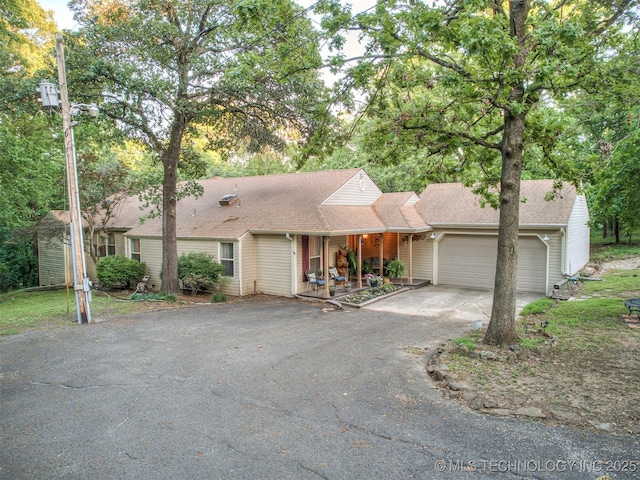 ranch-style house featuring asphalt driveway, a garage, a porch, and roof with shingles