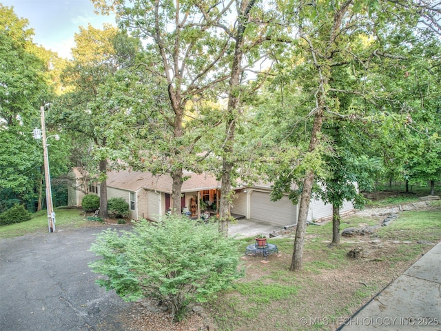 obstructed view of property featuring asphalt driveway, a garage, and a shingled roof