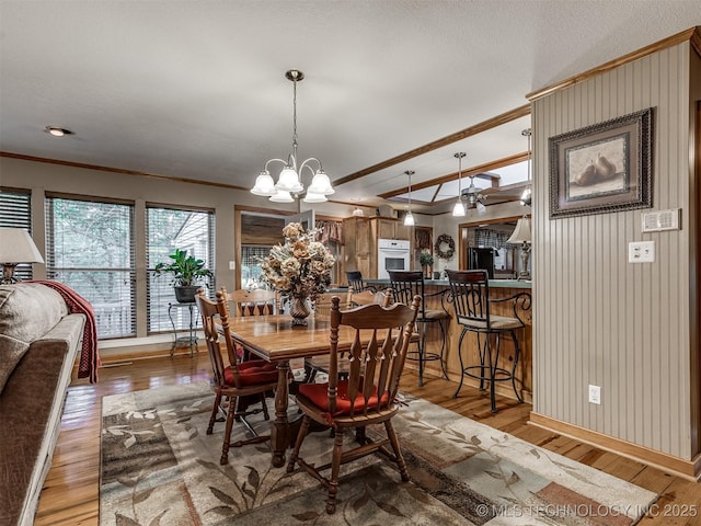 dining room featuring ornamental molding, wood finished floors, a chandelier, baseboards, and vaulted ceiling