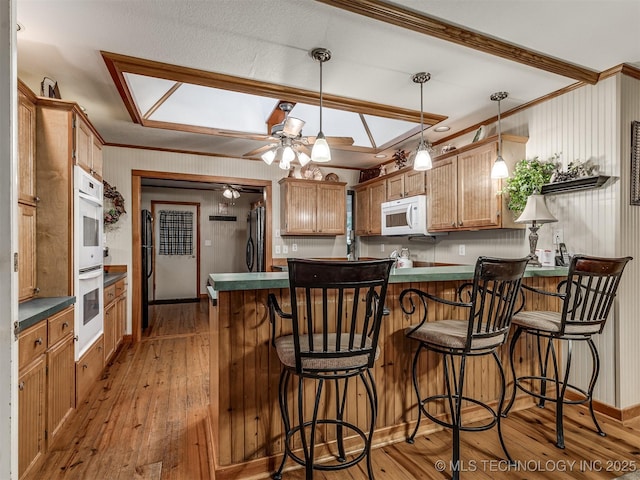 kitchen with crown molding, a peninsula, hardwood / wood-style flooring, white appliances, and dark countertops