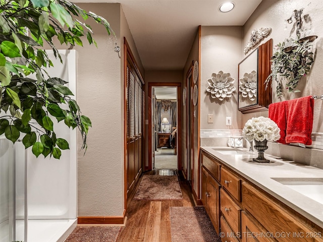 bathroom featuring wood finished floors, double vanity, baseboards, and a textured wall
