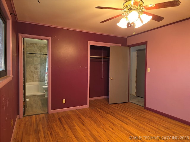unfurnished bedroom featuring wood finished floors, a closet, crown molding, ensuite bath, and baseboards