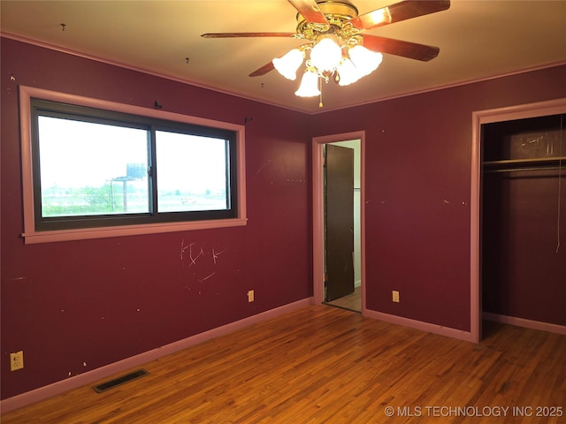 unfurnished bedroom featuring wood finished floors, ornamental molding, baseboards, a closet, and ceiling fan