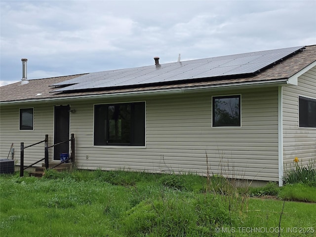 rear view of house featuring roof mounted solar panels and a shingled roof