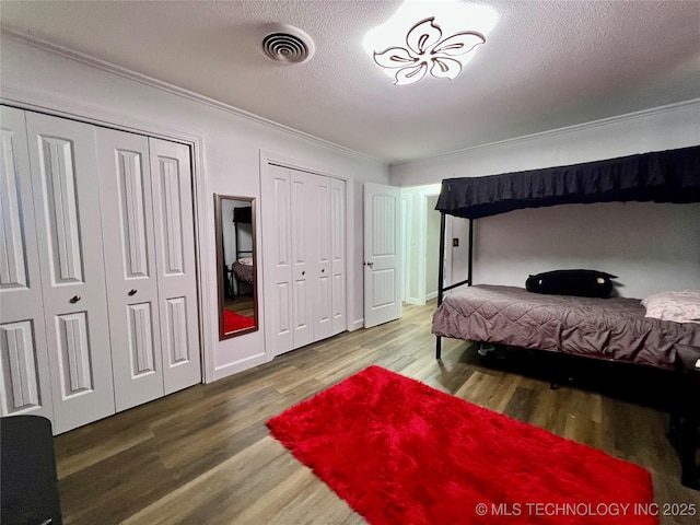 205 NE 1st St, Kingston, OK 73439 - bedroom with wood finished floors, ornamental molding, two closets, and a textured ceiling
