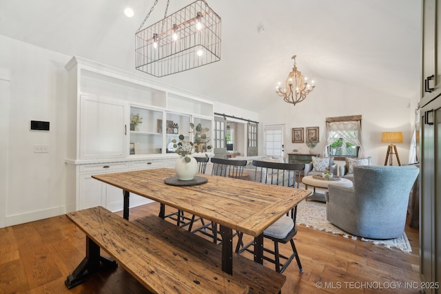 dining space with a chandelier, high vaulted ceiling, a barn door, baseboards, and wood finished floors
