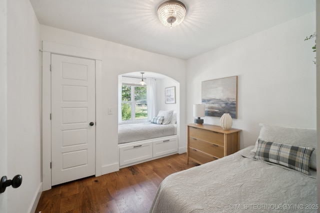 bedroom with arched walkways, dark wood-type flooring, and baseboards