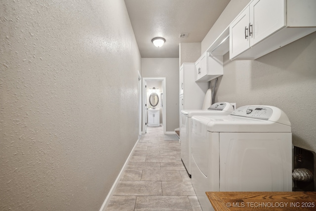 laundry area with a textured wall, washer and clothes dryer, cabinet space, and baseboards