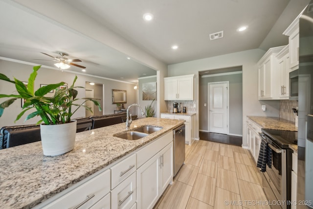 kitchen with appliances with stainless steel finishes, a sink, tasteful backsplash, white cabinetry, and light stone counters
