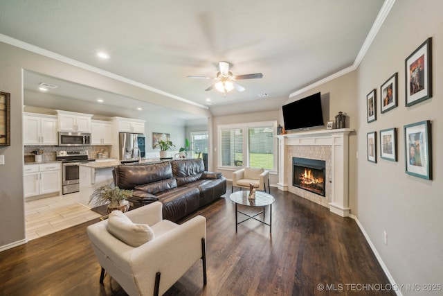 living room featuring a ceiling fan, wood finished floors, a tile fireplace, crown molding, and baseboards