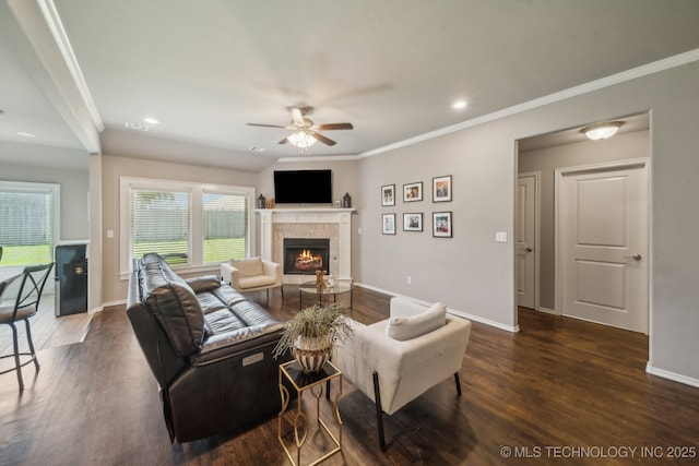 living area with ceiling fan, a tiled fireplace, dark wood-style floors, baseboards, and ornamental molding