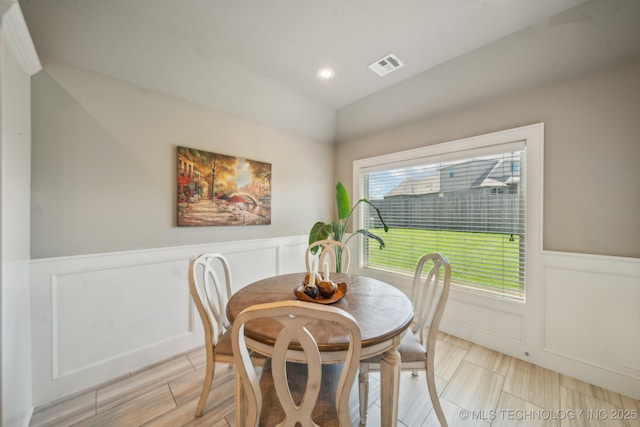 dining area featuring wainscoting, a decorative wall, and lofted ceiling