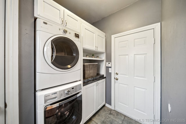 clothes washing area with cabinet space, stacked washer and clothes dryer, and dark tile patterned flooring