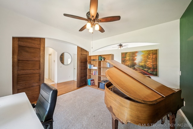 carpeted office space featuring ceiling fan, arched walkways, and baseboards