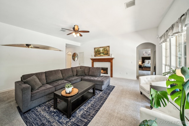 carpeted living room featuring a ceiling fan, arched walkways, a lit fireplace, and baseboards