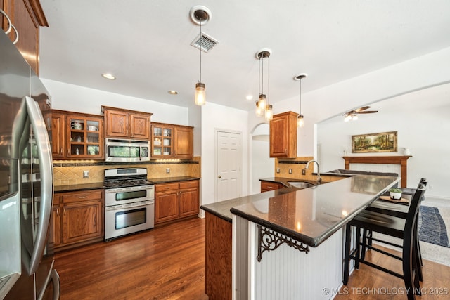 kitchen featuring stainless steel appliances, brown cabinets, ceiling fan, backsplash, and a kitchen breakfast bar